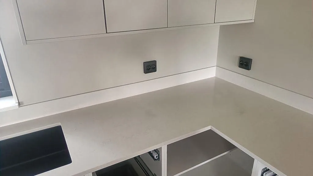 Hörnmonterad köksbänkskiva i polerad Silestone Linen Cream med låg stänkkant och beige ådring i Tågarp.