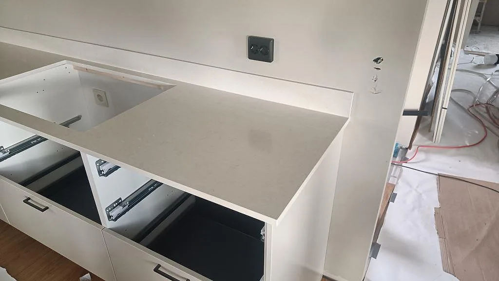 Polerad Silestone Linen Cream som köksbänkskiva med stort rektangulärt urtag och öppen stomme under montering i Tågarp.