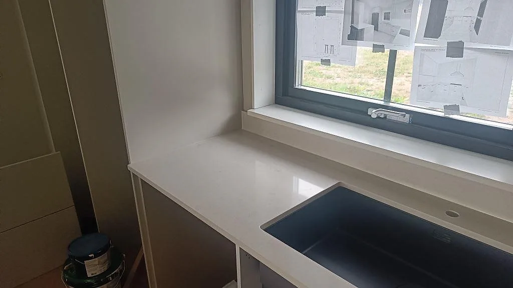 Köksbänkskiva i polerad Silestone Linen Cream med låg stänkkant, fönsterparti och rektangulärt urtag i Tågarp.