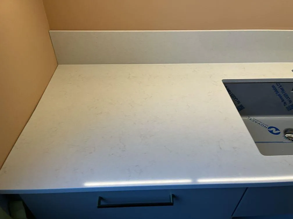 Polerad Silestone Linen Cream bänkskiva med underlimmad diskho och uppvikt stänkkant mot grundmålad vägg i ett kök i Täby.