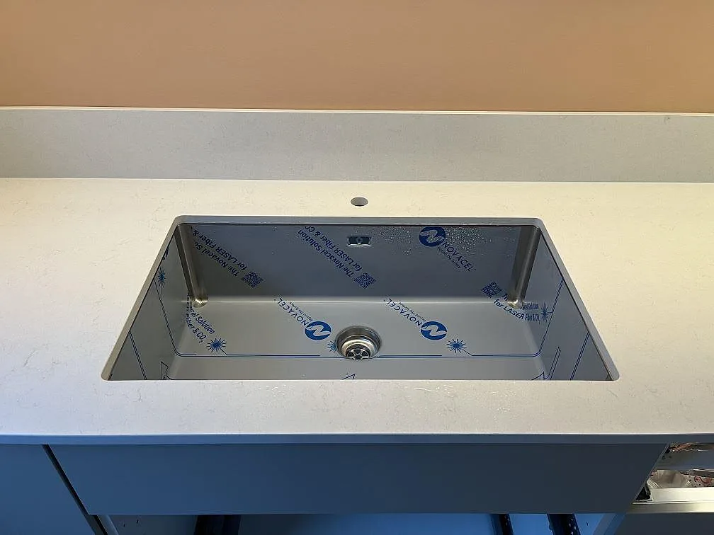Underlimmad rostfri diskho i en polerad Silestone Linen Cream köksbänkskiva med separat blandarhål i Täby.