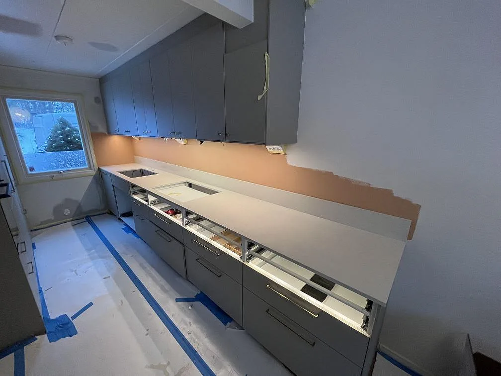 Köksbänkskiva i krämfärgad Silestone Linen Cream, polerad, monterad längs en enkelvägg under grå överskåp i ett kök under montering i Täby.