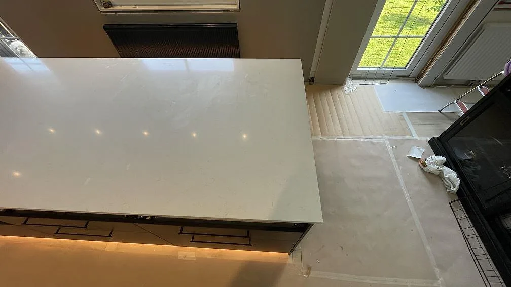 Polerad kompositbänkskiva i Silestone Linen Cream på en lång köksö i Tomelilla, fotograferad uppifrån under montering.
