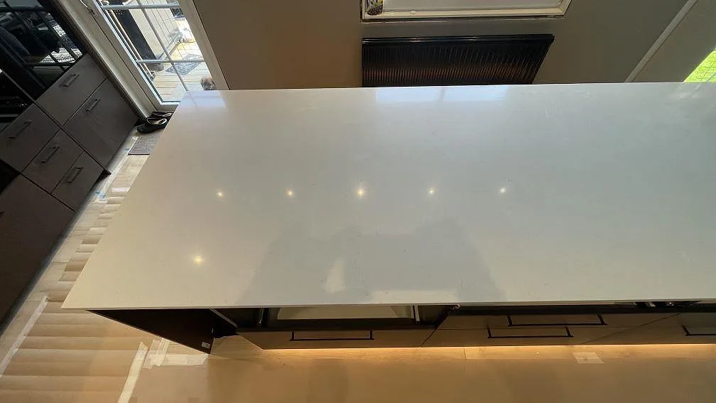 Stor köksö i Silestone Linen Cream, polerad komposit, med ljus yta och mörka köksstommar i Tomelilla.