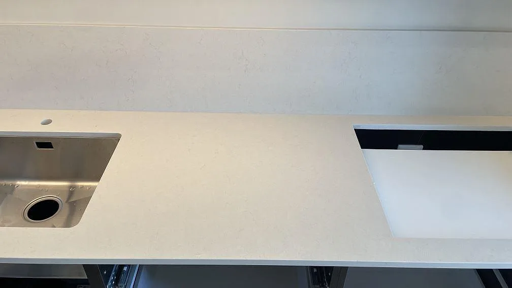 Polerad Silestone Linen Cream i Tomelilla med rostfri diskho, hällöppning och ljust stänkskydd längs köksväggen.