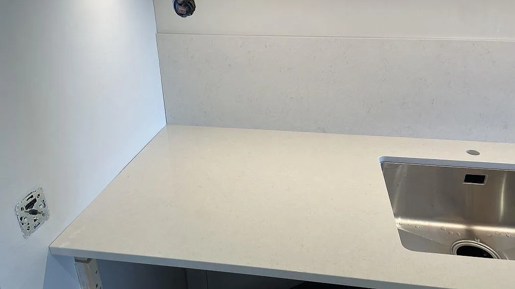 Detalj av polerad Silestone Linen Cream med rostfri diskho, kranhål och stänkskydd i Tomelilla.