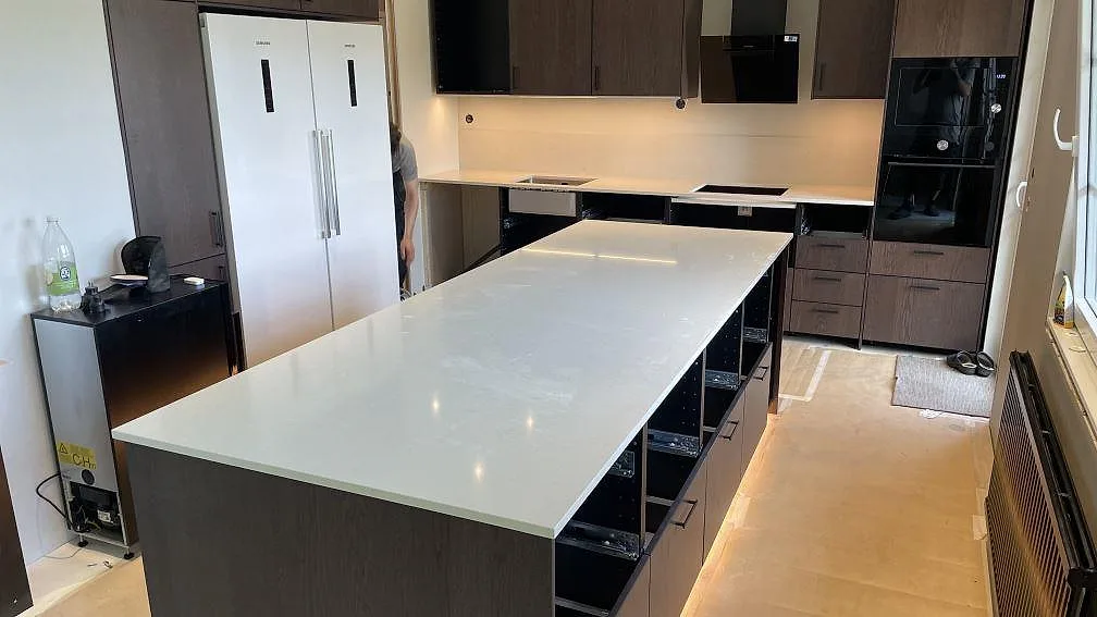 Kök i Tomelilla med polerad Silestone Linen Cream som ljus kompositbänkskiva, stor köksö, väggbänk, diskho och hällöppning.