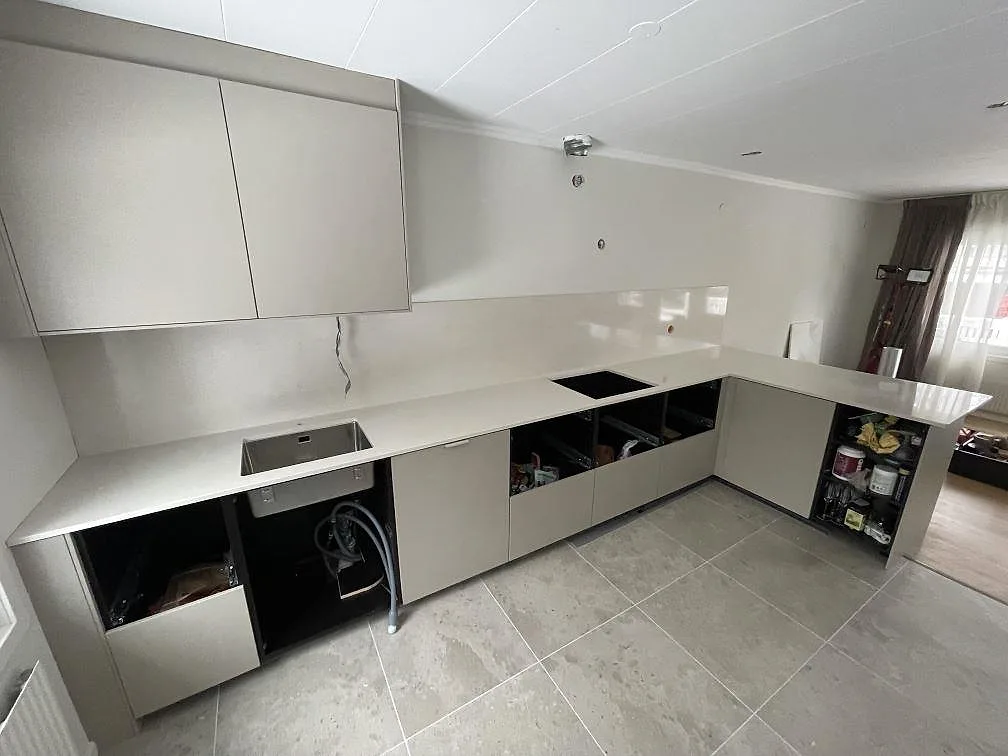 Polerad köksbänkskiva i Silestone Linen Cream längs väggen i ett kök i Tumba, med underlimmad rostfri diskho, hällurtag och halvö under montering.