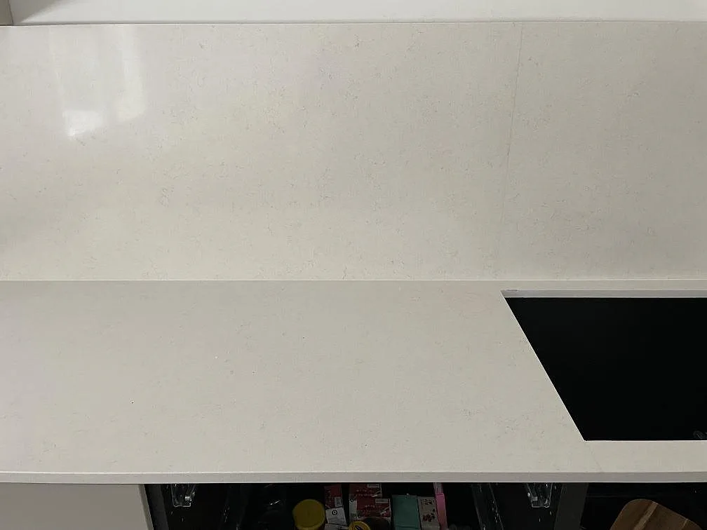Bänkyta och uppvikt stänkkant i polerad Silestone Linen Cream med hällurtag i ett kök i Tumba, där den ljusa kompositens diskreta ådring syns.