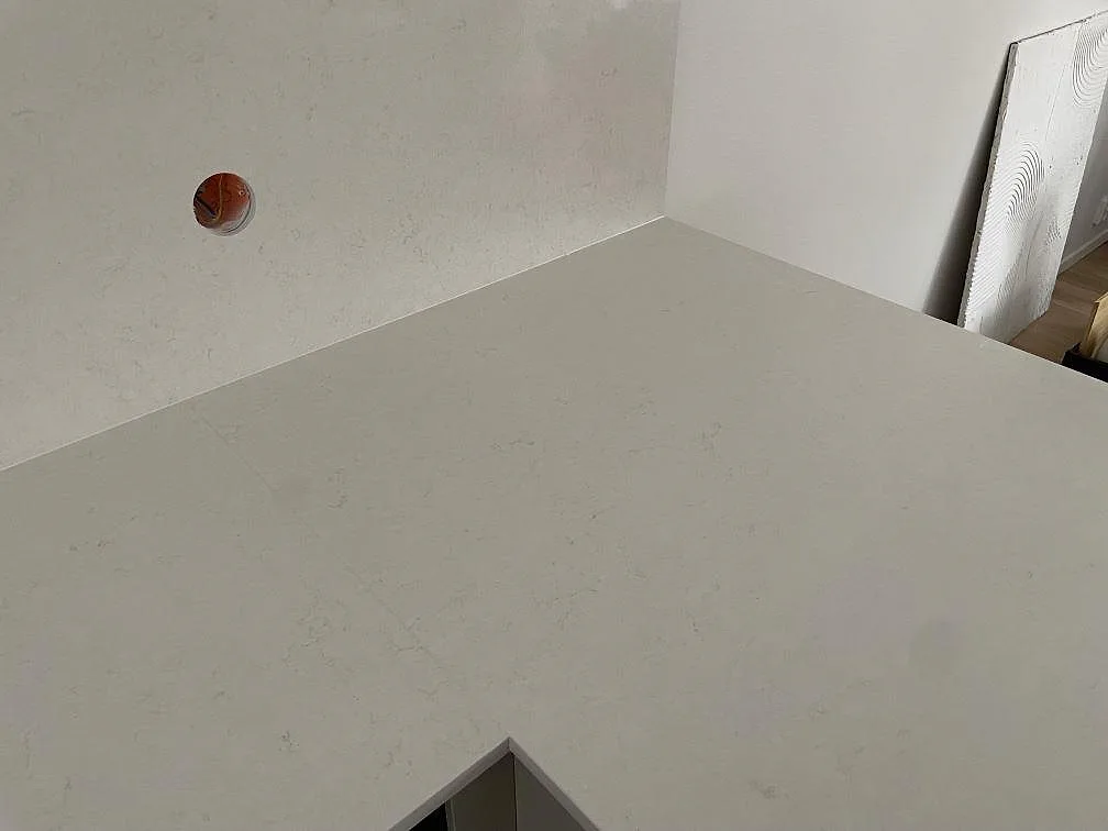Halvöns hörn i polerad Silestone Linen Cream med uppvikt stänkkant i ett kök i Tumba, med den krämvita kompositens mjuka ton.