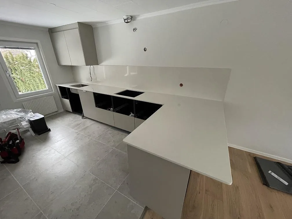 Köksbänkskiva i Silestone Linen Cream, polerad, i ett U-format kök i Tumba med lång vinklad halvö, urtag för diskho och häll samt uppvikt stänkkant.
