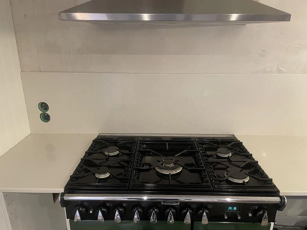 Fristående spis i hörnet med köksbänkskiva och uppvikt stänkkant i Silestone Linen Cream, polerad, i ett kök i Värmdö.