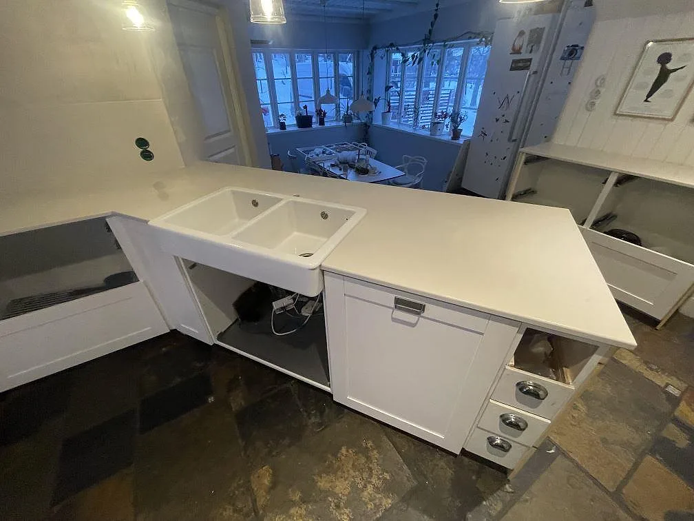 Polerad köksbänkskiva i ljus Silestone Linen Cream med underlimmad vit dubbelho och skiffergolv i ett kök i Värmdö.