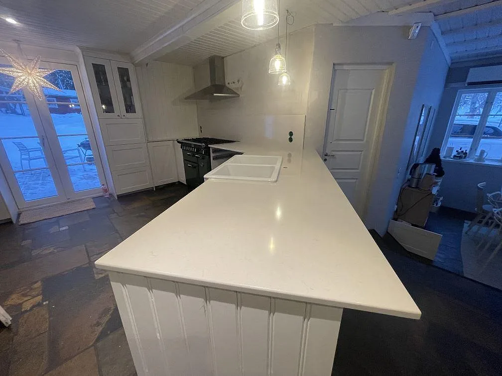 Köksbänkskiva i Silestone Linen Cream, polerad, som löper runt en hörnhalvö med panelad framsida i ett kök i Värmdö.