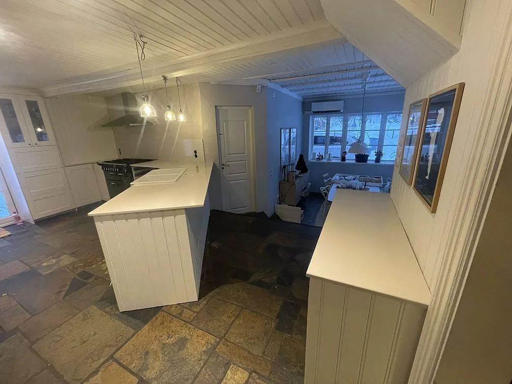 Vidvinkel av kök i Värmdö med halvö och bakre bänk i Silestone Linen Cream, polerad, mot ljusa panelväggar.