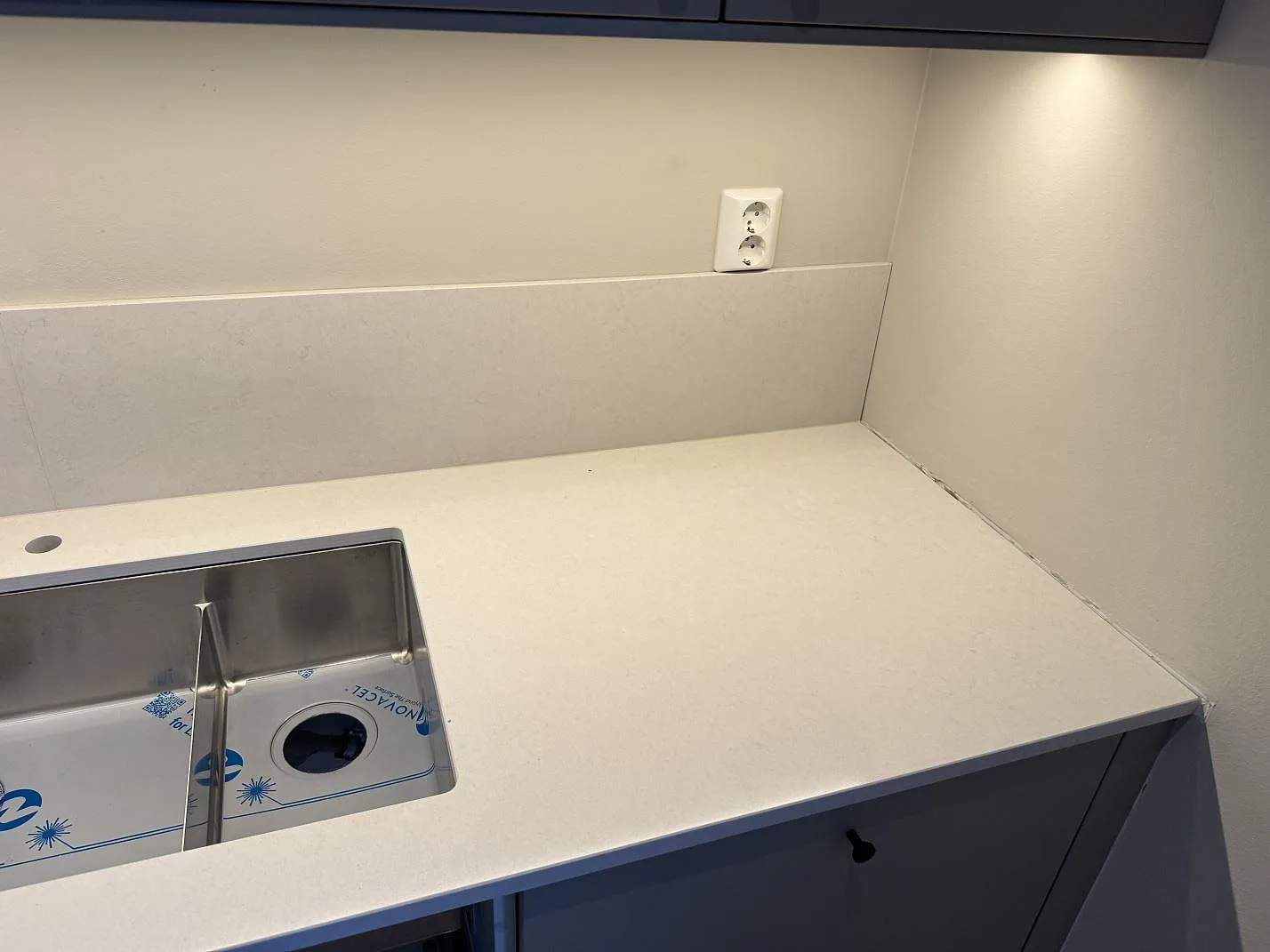 Underlimmad rostfri diskho med slipat blandarhål i polerad Silestone Linen Cream köksbänkskiva i ett kök i Växjö.