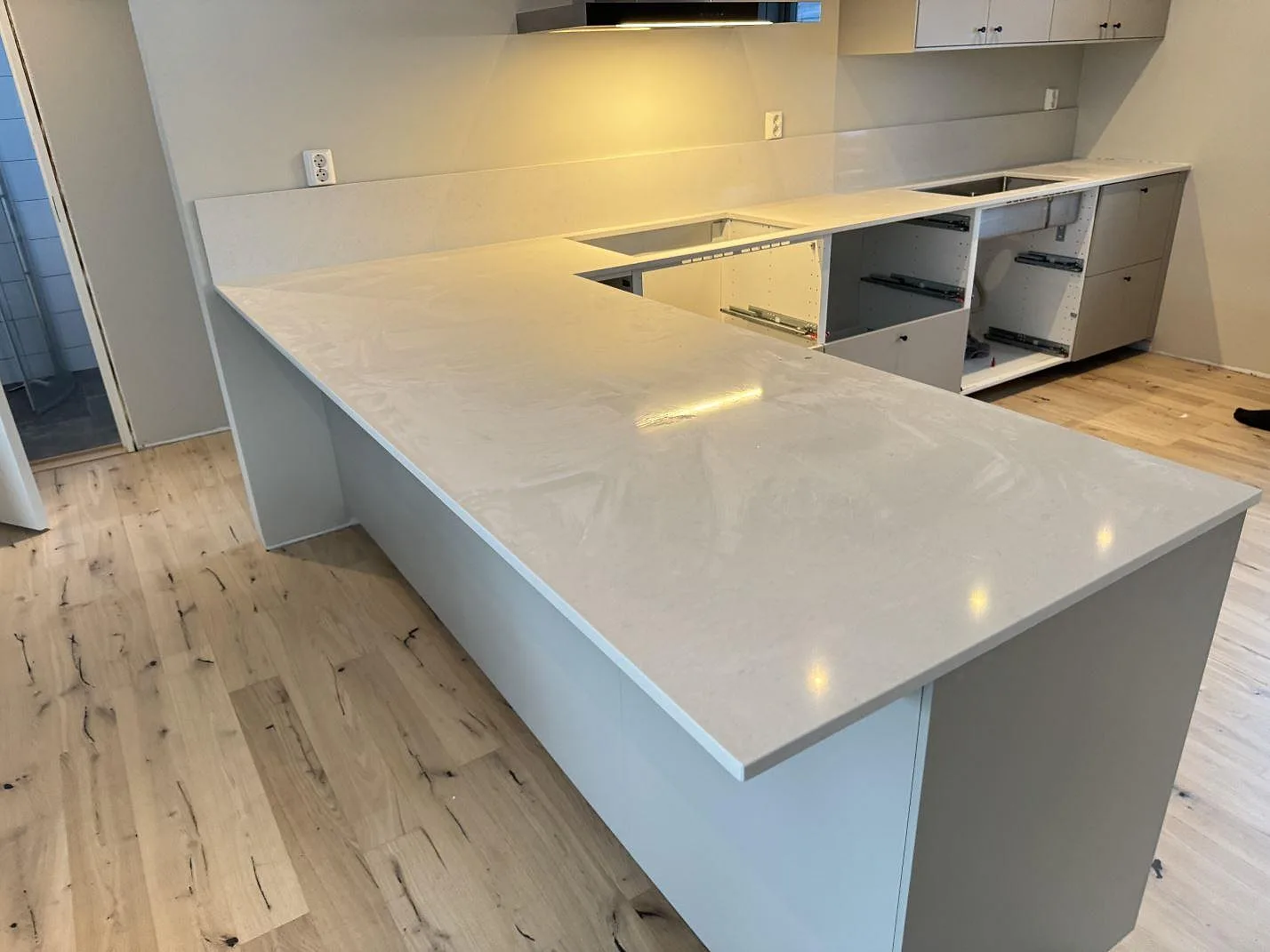 Köksbänkskiva i polerad Silestone Linen Cream i ett vinklat kök med halvö och bardel i Växjö, sedd i rummet under montering.