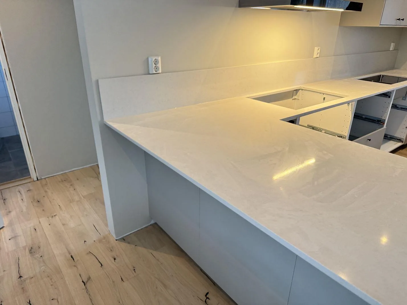 Gräddvit Silestone Linen Cream köksbänkskiva i Växjö med halvö, urtag för induktionshäll och uppvikt stänkkant, eye-level under montering.