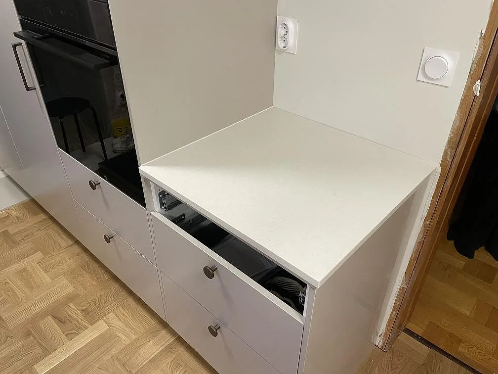 Sidobänk i polerad Silestone Linen Cream intill ugnsskåp och öppna lådstommar i ett kök under montering i Valbo.