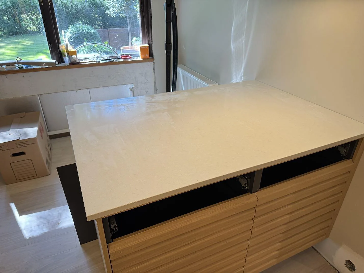 Bred köksbänkskiva i polerad Silestone Linen Cream, ljus kvartskomposit, på träinredning i ett kök under montering i Veberöd.