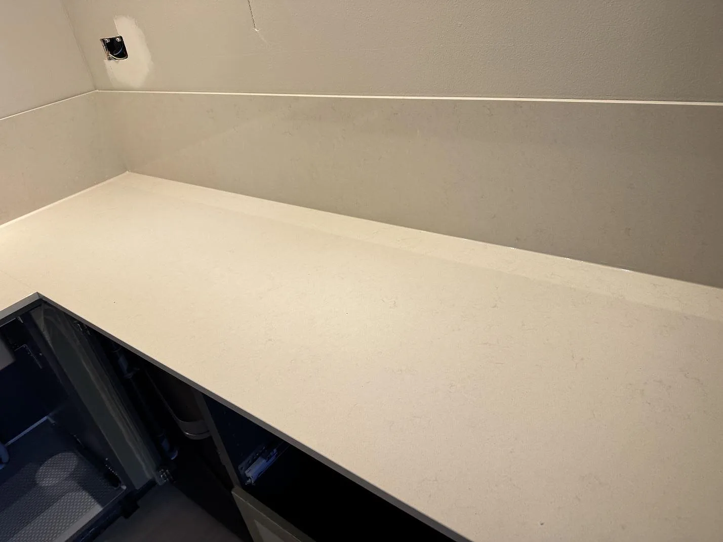 Installerad köksbänkskiva i Silestone Linen Cream, polerad kvartskomposit, över öppna köksstommar med vägguttag ovanför i Veberöd.