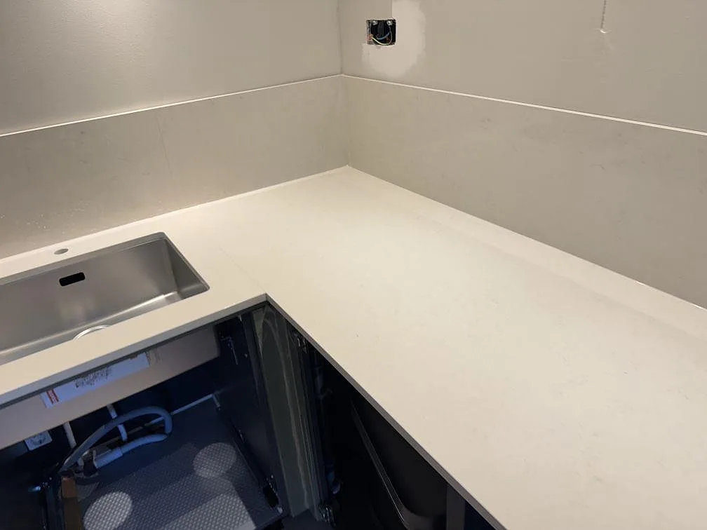 Ljus köksbänkskiva i polerad Silestone Linen Cream med matchande stänkkant längs väggen i ett kök i Veberöd.
