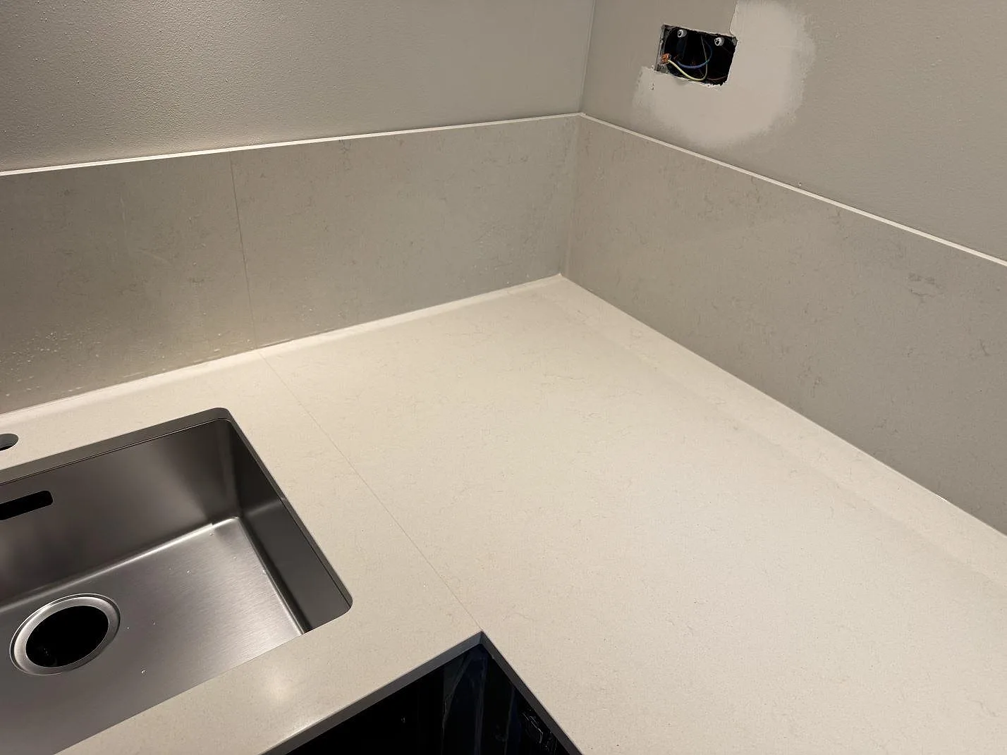 Polerad Silestone Linen Cream köksbänkskiva med rostfri diskho, låg stänkkant och öppna köksstommar under montering i Veberöd.