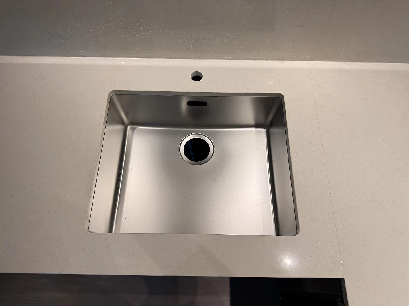 Närbild på rostfri diskho monterad under en polerad Silestone Linen Cream-bänkskiva med blandarhål i ett kök i Veberöd.