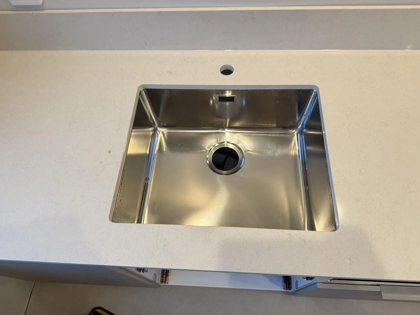 Närbild på rostfri diskho monterad under en polerad Silestone Linen Cream bänkskiva med blandarhål i Vintrie.