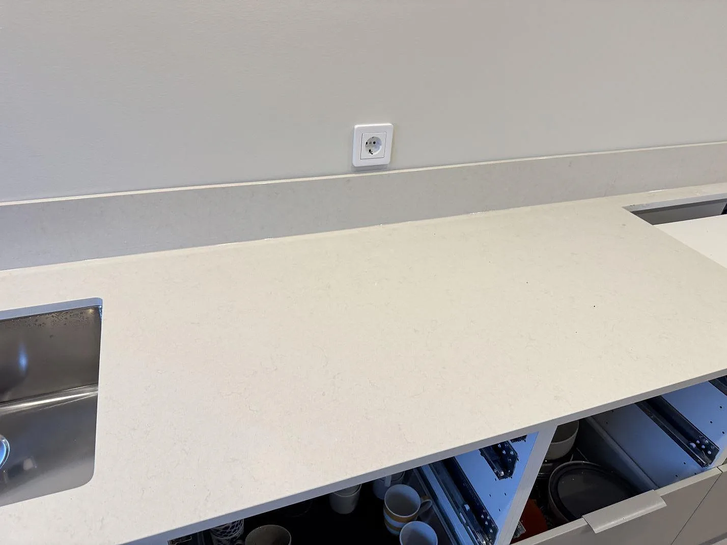 Lång bänkyta i polerad Silestone Linen Cream med stänkskydd, diskho i kanten och öppna köksstommar i Vintrie.