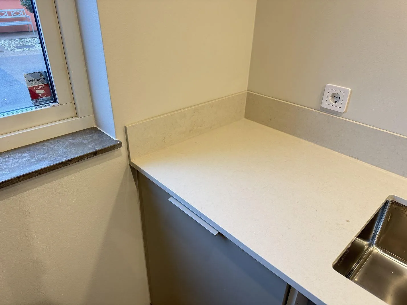 Ljus köksbänkskiva i polerad Silestone Linen Cream med rostfri underlimmad diskho och stänkskydd vid fönster i Vintrie.