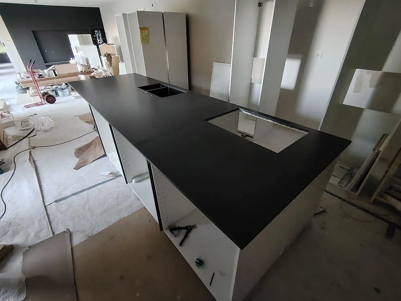 Köksbänkskiva och köksö i mörkgrå Silestone Marengo komposit, 20 mm Mocka, med induktionshäll i ett kök under montering i Borensberg.