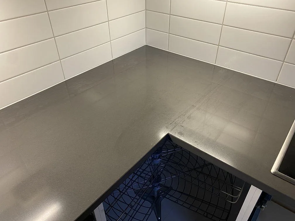 Köksbänkskiva i mörkgrå Silestone Marengo, polerad, monterad i hörn mot vitt kakel i ett kök i Falkenberg.