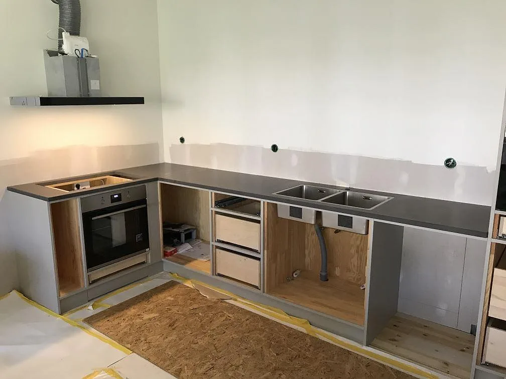 Köksbänkskiva i grå komposit Silestone Merope, matt yta, med inbyggd ugn och underlimmad rostfri dubbelho i ett L-format kök under montering i Stenkullen.