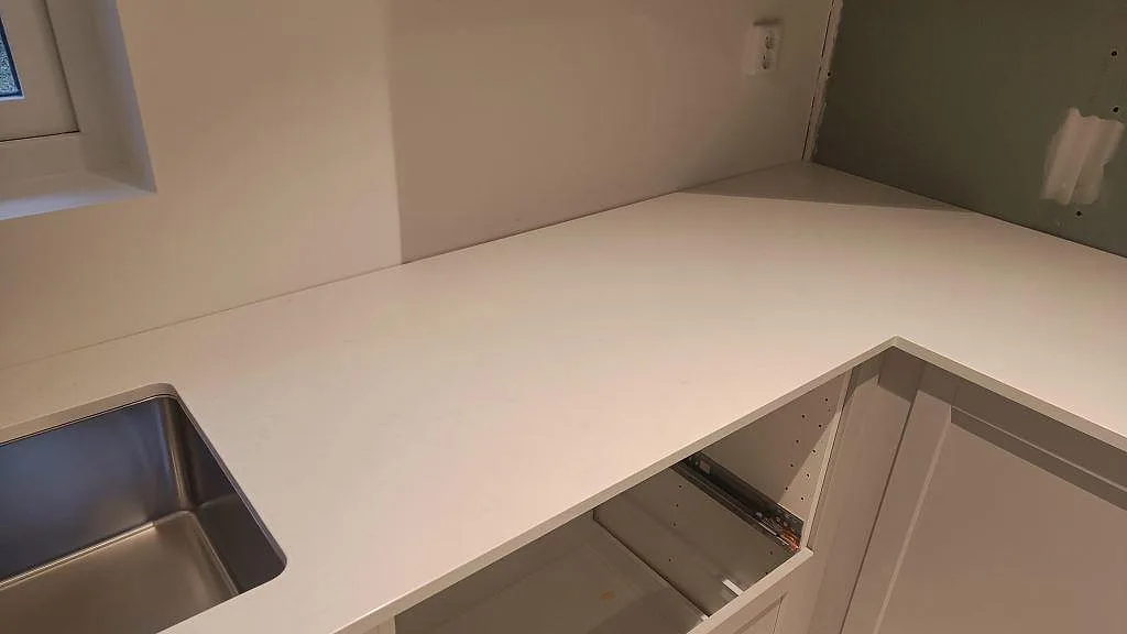 Hörndel av vit Silestone Miami Vena köksbänkskiva under montering vid diskho och vägg i Höllviken.