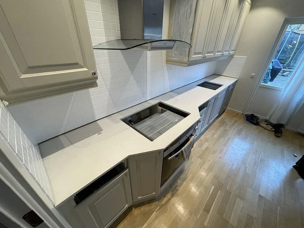 Köksbänkskiva i vit Silestone Miami Vena, polerad kvartskomposit, monterad längs en vinklad skåprad i ett kök i Huddinge.
