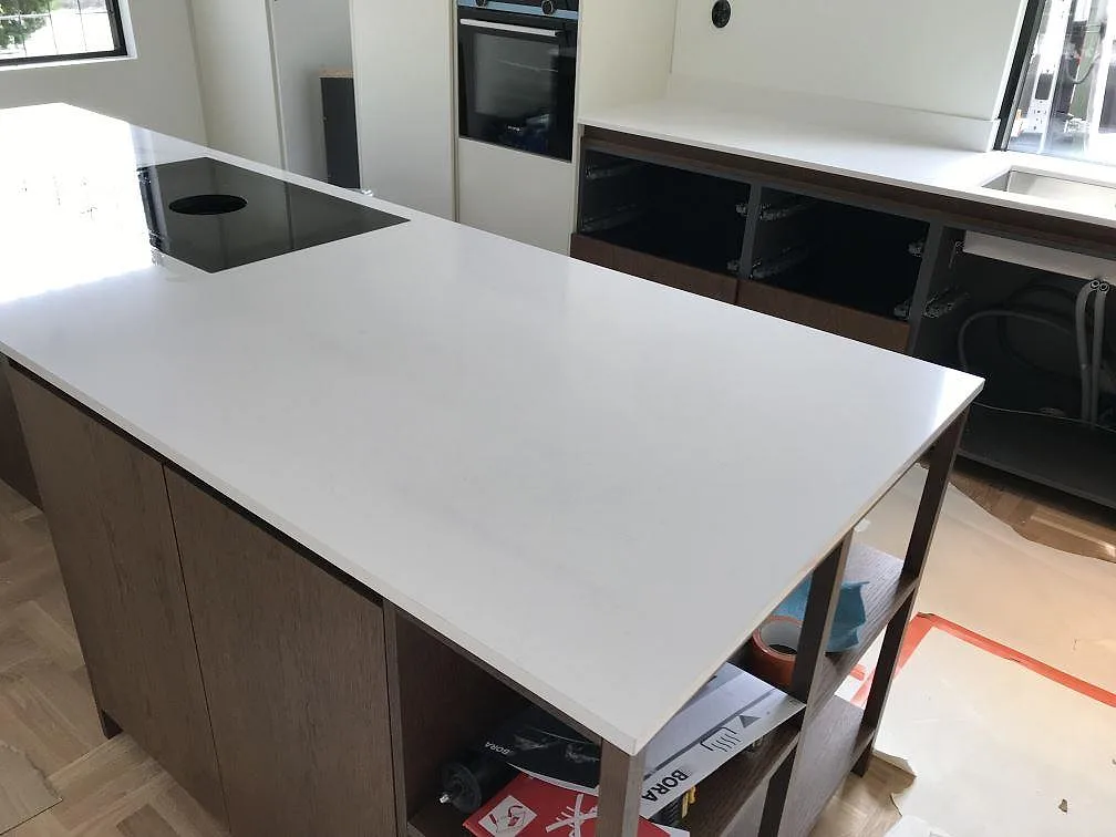 Köksö i vit Silestone Miami Vena med fin grå ådring och inbyggd svart induktionshäll, eye-level vy i ett kök under montering i Karlshamn.
