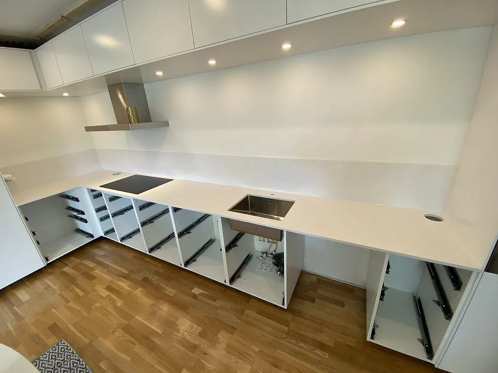 Köksbänkskiva i vit Silestone Miami Vena, polerad, längs ett L-format kök i Lund med underlimmad rostfri diskho, induktionshäll och stänkskydd i samma sten, fotograferat under montering.
