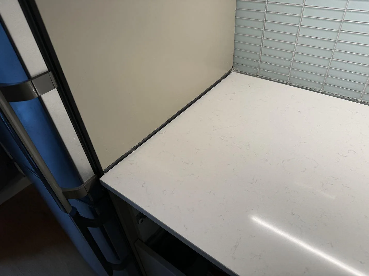 Närbild på änden av polerad Silestone Miami Vena köksbänkskiva i Malmö, monterad mot vägg och kylskåp med diskret grå ådring.
