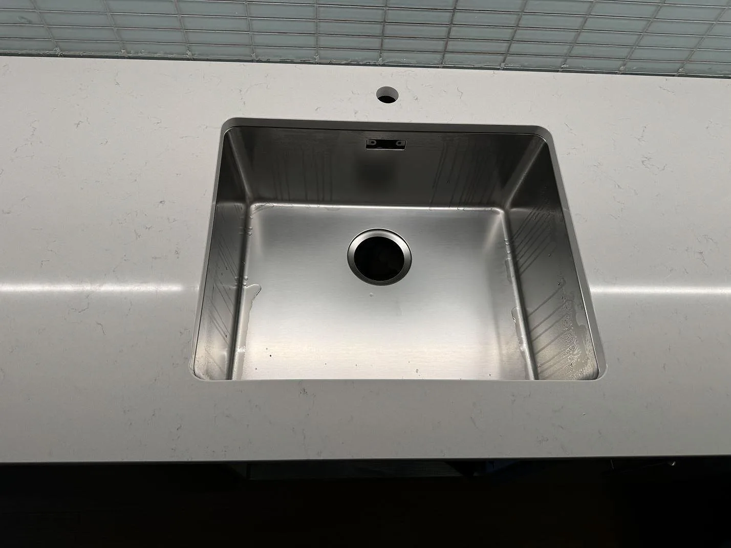 Närbild på rostfri diskho i polerad Silestone Miami Vena köksbänkskiva i Malmö, med kranhål bakom hon och ljus komposityta.