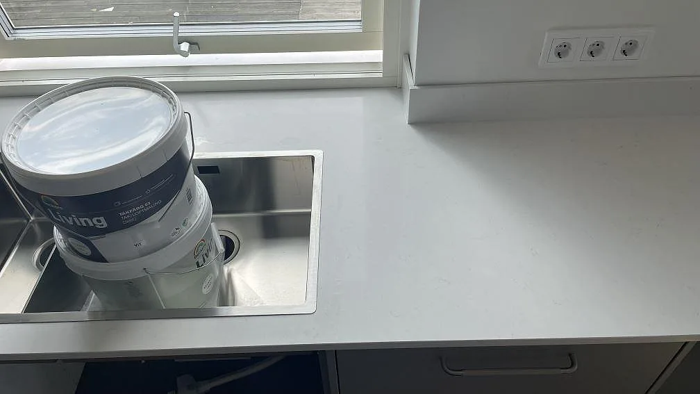 Närbild på underlimmad rostfri diskho och vit polerad Silestone Miami Vena i ett kök under montering i Mölndal.