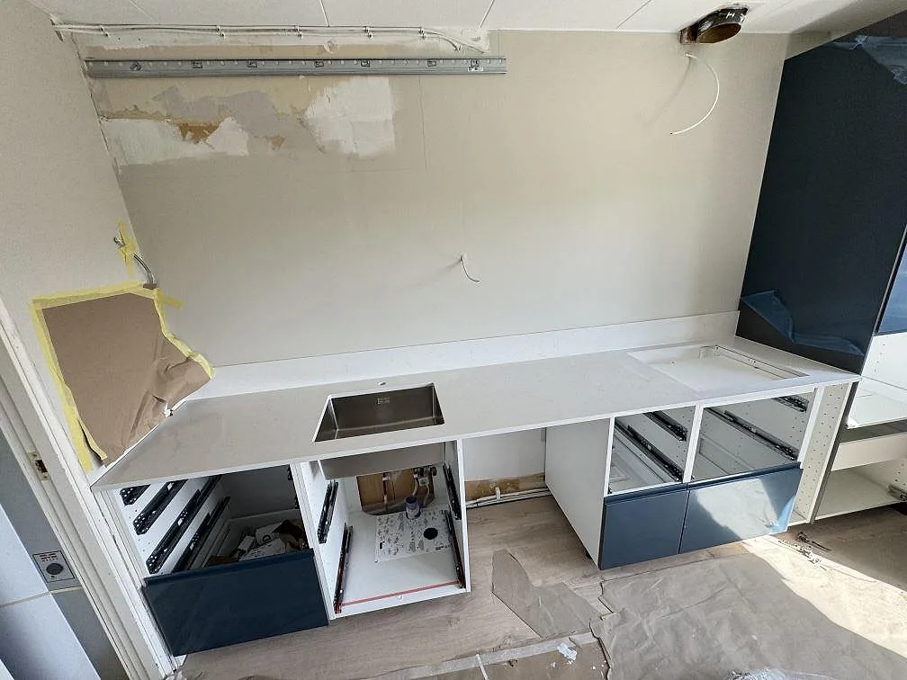 Köksbänkskiva i polerad Silestone Miami Vena, vit kvartskomposit med låg stänkkant och rostfri diskho under montering i Staffanstorp.
