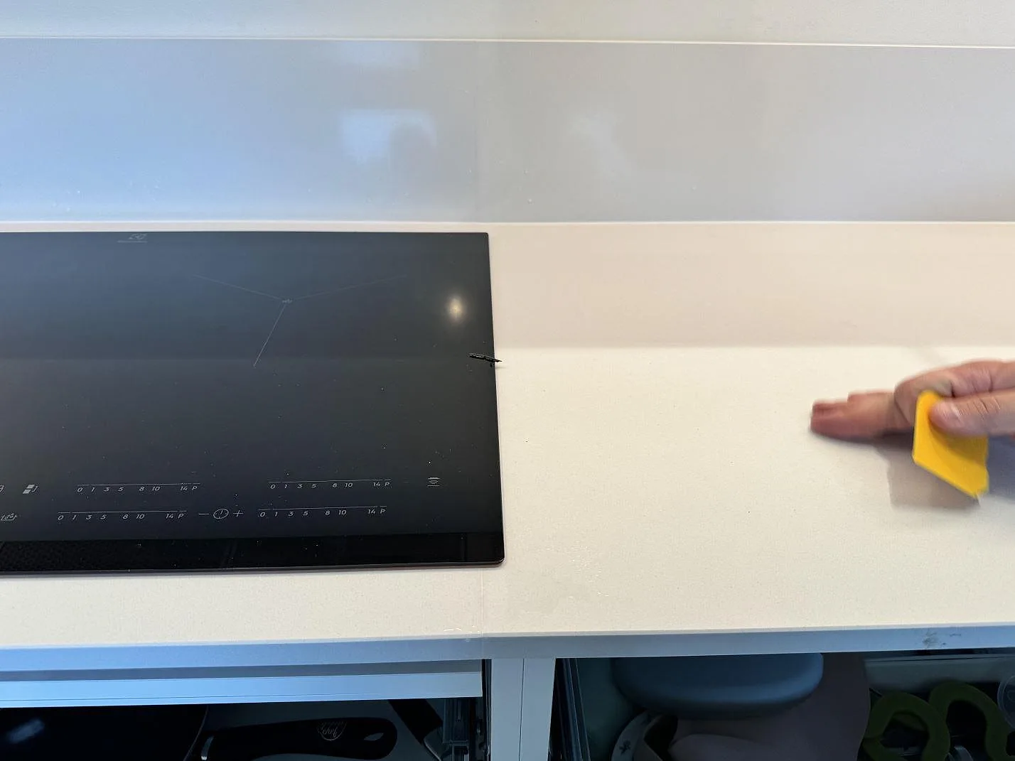 Installationsdetalj där en polerad Silestone Miami White bänkskiva rengörs intill svart häll i köket i Bunkeflostrand.