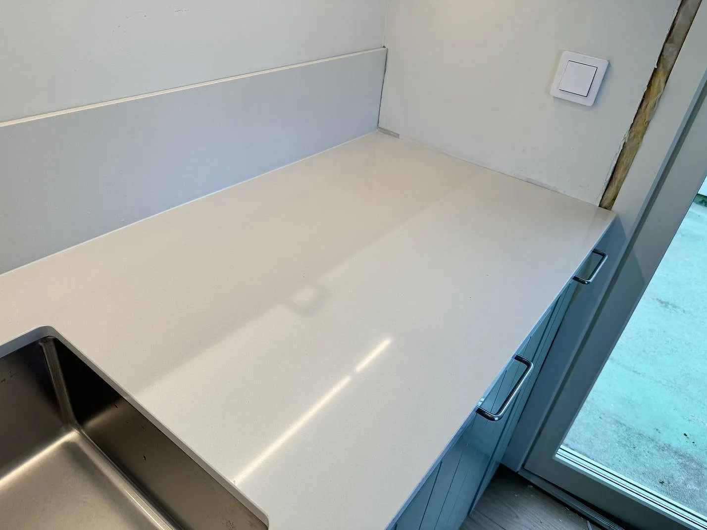 Vit polerad Silestone Miami White köksbänkskiva vid den rostfria diskhon och altandörren i ett kök i Bunkeflostrand.