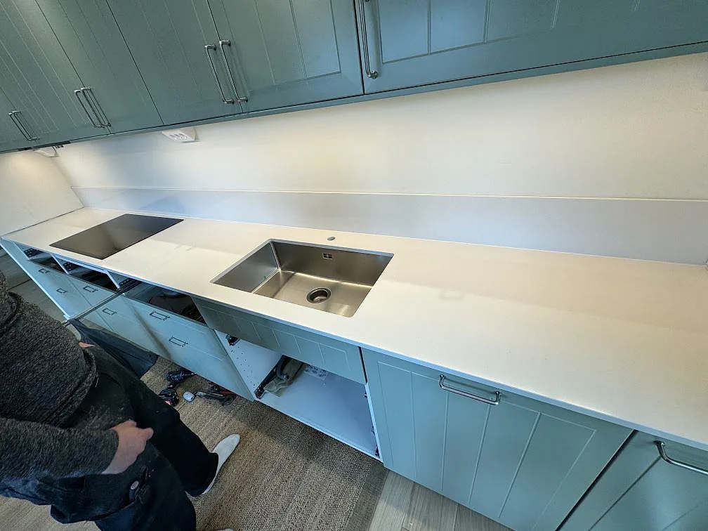 Köksbänkskiva i vit polerad Silestone Miami White med underlimmad rostfri diskho, svart häll och stänkskydd i ett kök i Bunkeflostrand.