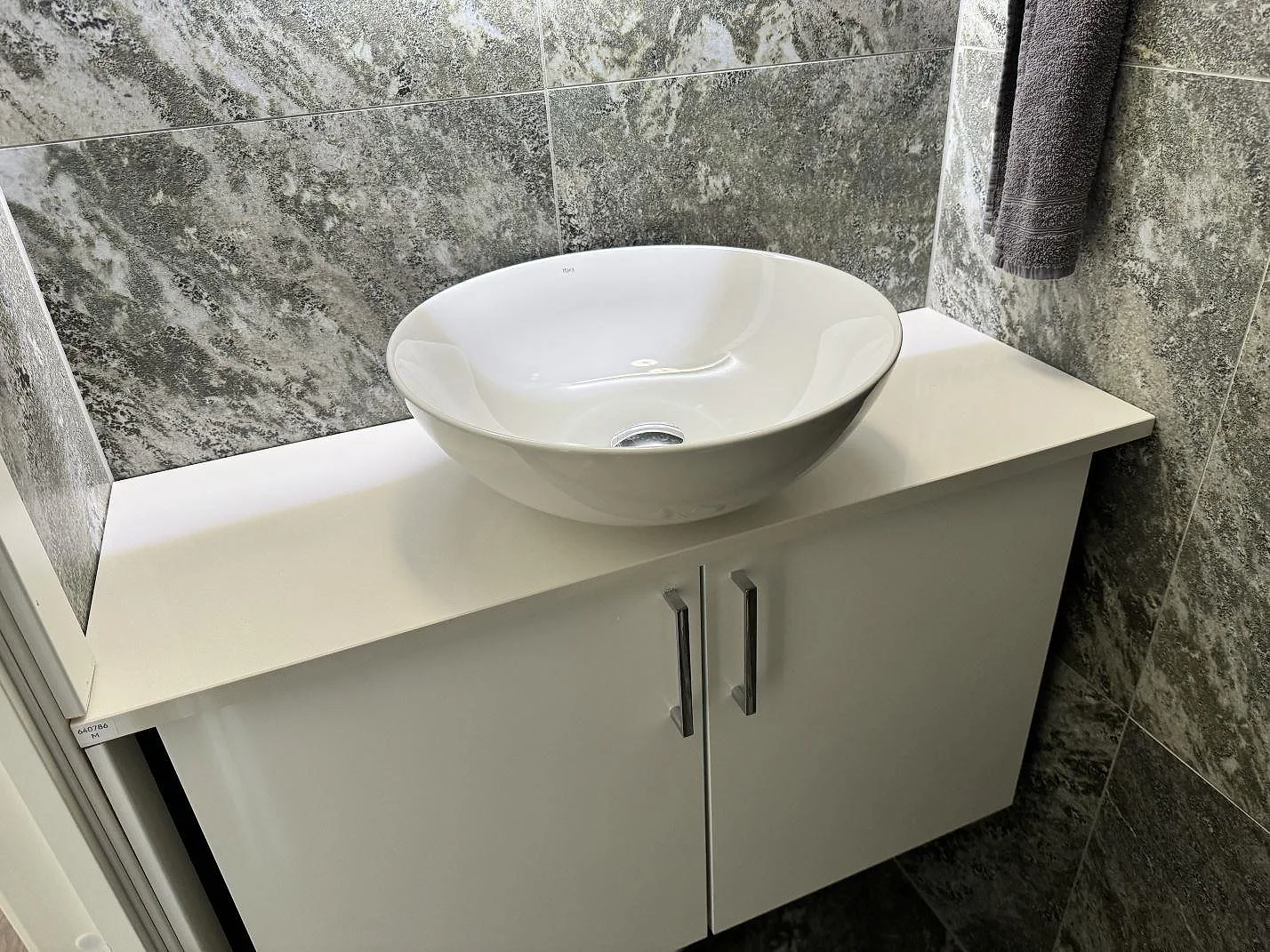 Badrumsbänkskiva i vit polerad Silestone Miami White med runt ovanpåliggande tvättställ och grå kakelvägg i Bunkeflostrand.