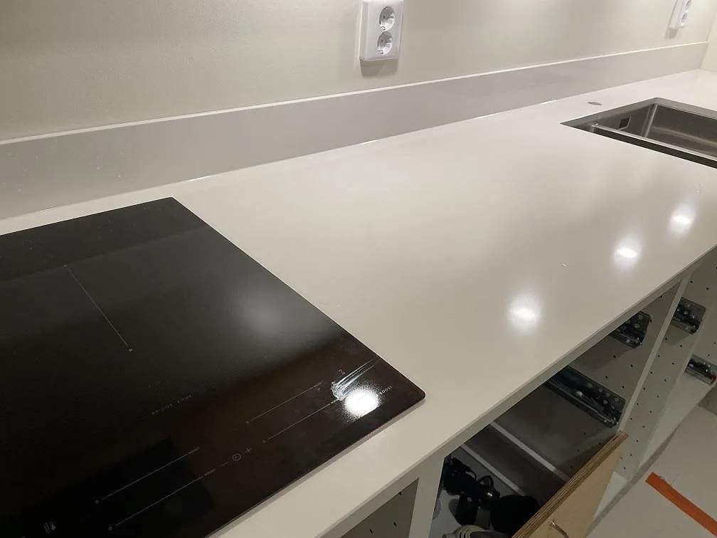 Närbild på polerad Silestone Miami White bänkskiva i komposit med svart induktionshäll, rostfri diskho och låg stänkkant i ett kök i Göteborg.