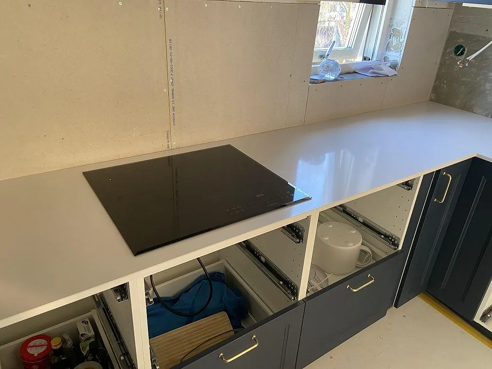 Köksbänkskiva i vit Silestone Miami White, polerad kvartskomposit, med övermonterad svart induktionshäll i ett kök under montering i Helsingborg.
