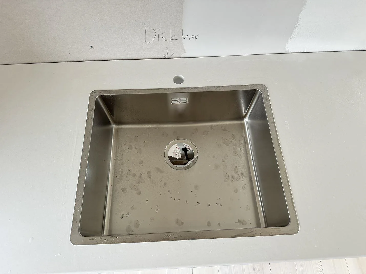 Närbild på rostfri diskho och blandarhål i polerad Silestone Miami White, vit kvartskompositbänkskiva i Jönköping.
