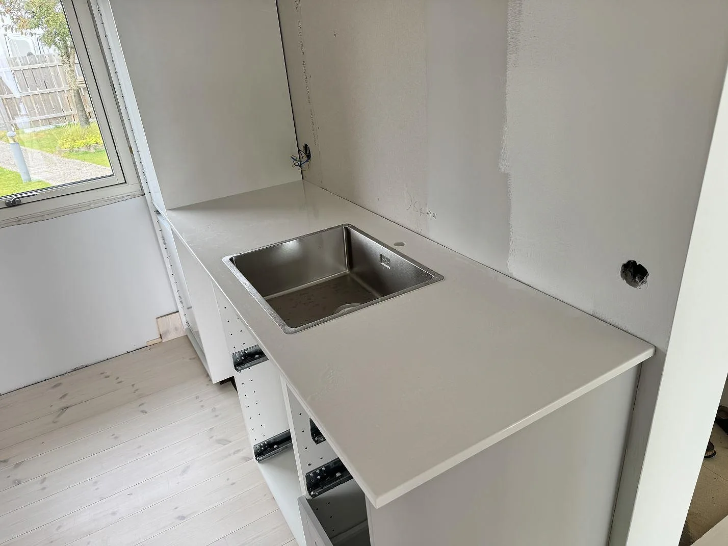 Köksbänkskiva i vit Silestone Miami White, polerad kvartskomposit, med rostfri diskho i ett kök under montering i Jönköping.